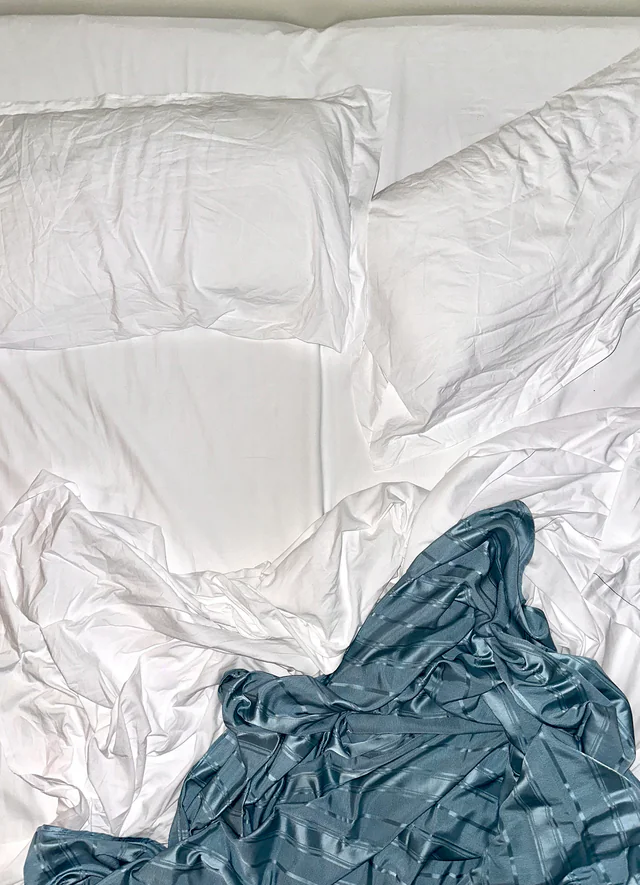 An unmade bed seen from above: white sheets and pillows, a blue blanket